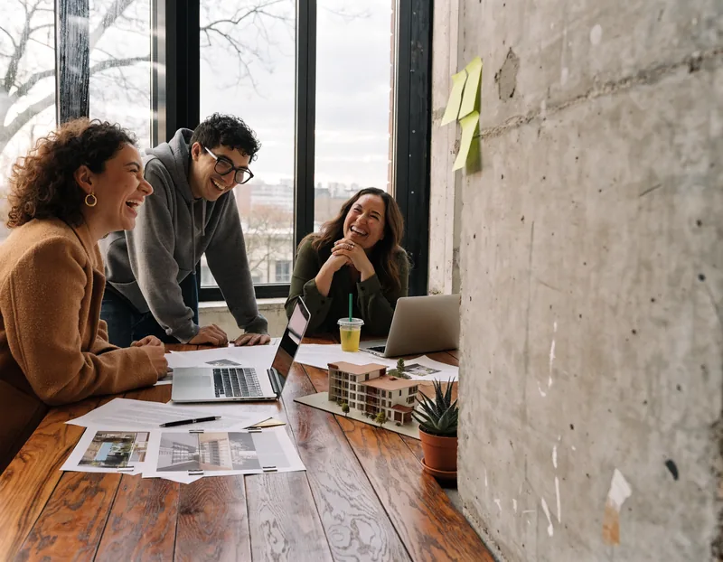 Tres colegas del equipo riendo alrededor de una maqueta y renders en una sala de ventas